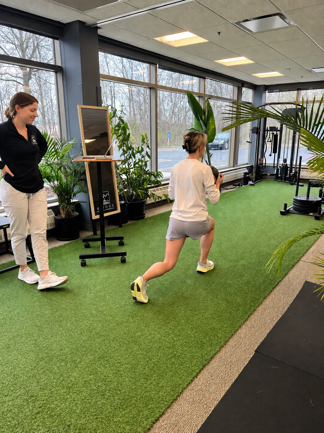 Bridge physical therapist coaching an athlete through a reverse lunge with a medicine ball