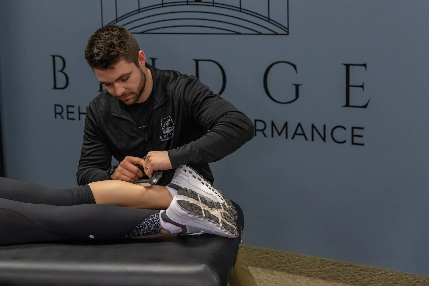 Bridge physical therapist performing instrument-assisted soft tissue work on an athlete's calf